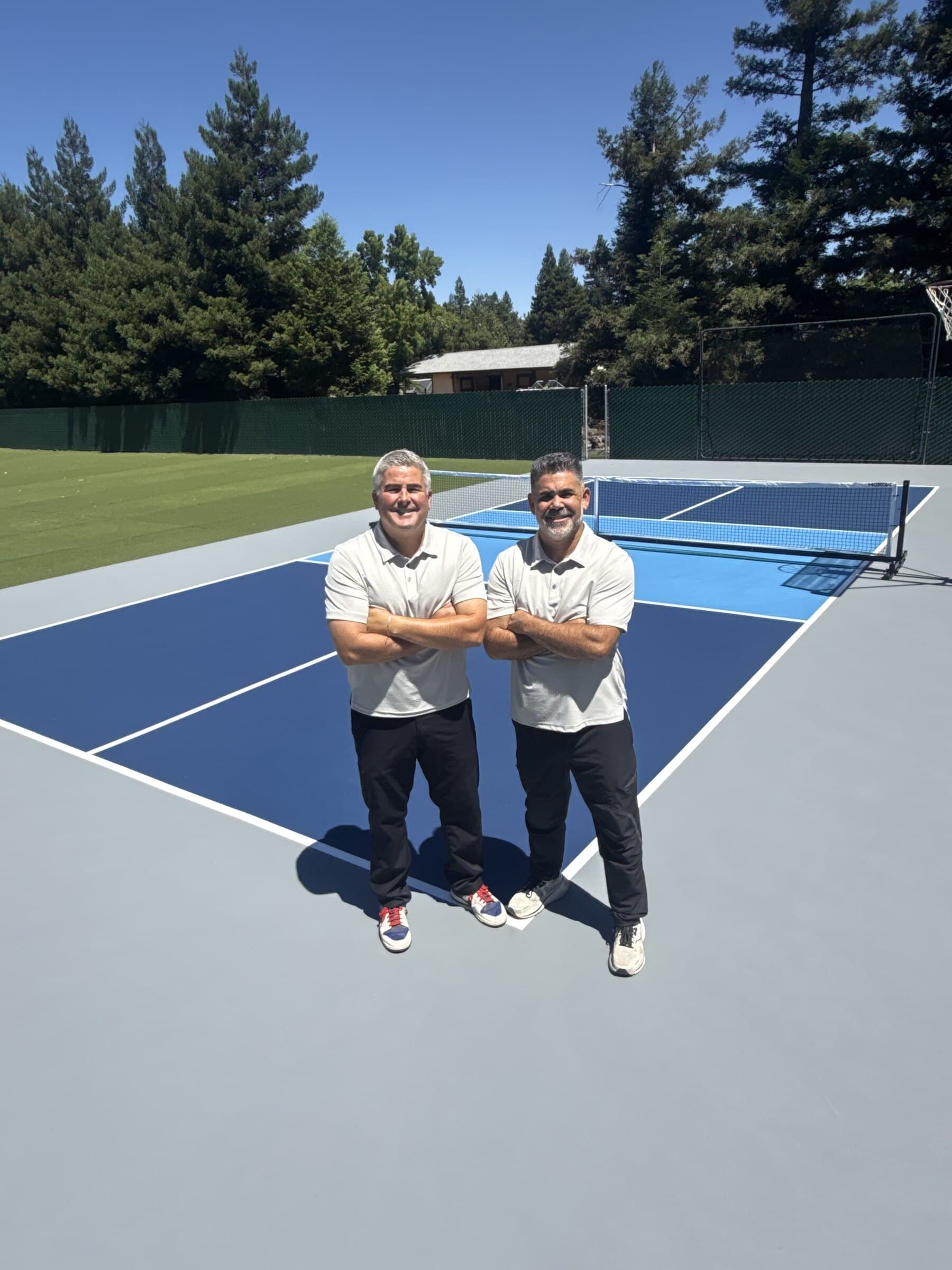 The two owners of NorCal Surfaces standing on a blue pickleball court they built